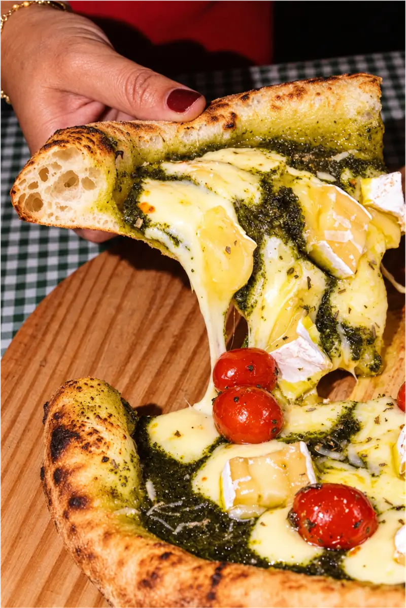 Slice of Neapolitan pizza with pesto, brie and confit tomato, airy raised crust